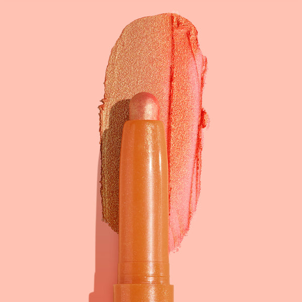 ColourPop Shadow Stix Friday Feels glides a metallic peach-coral swipe across a blush-pink background, showcasing the creamy twist-up eyeshadow crayon and its shimmery finish.