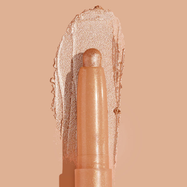 Honey BB ColourPop Shadow Stix crayon swipes a warm honey-gold metallic eyeshadow, with a creamy reflective swatch and fine sparkle catching light against a nude peach background.