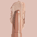Socialite ColourPop Shadow Stix glides a metallic champagne‑rose swipe across a nude backdrop, twist‑up cream eyeshadow stick shown close up to highlight smooth, blendable texture and high‑shine shimmer for quick eyelid application.