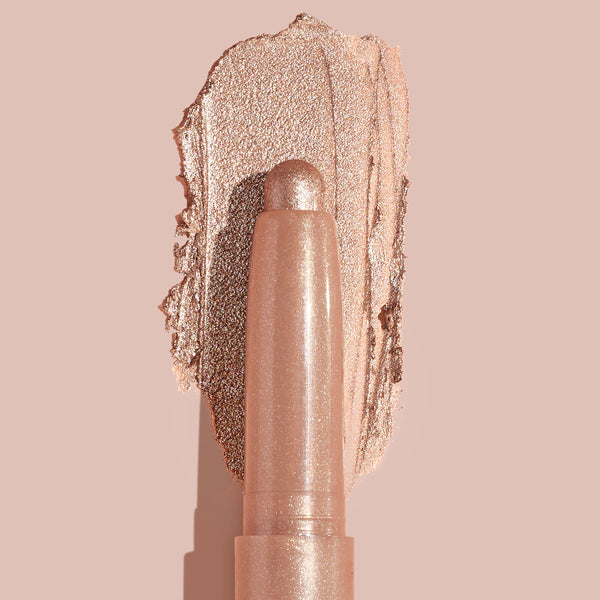 Socialite ColourPop Shadow Stix glides a metallic champagne‑rose swipe across a nude backdrop, twist‑up cream eyeshadow stick shown close up to highlight smooth, blendable texture and high‑shine shimmer for quick eyelid application.