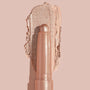 Socialite ColourPop Shadow Stix glides a metallic champagne‑rose swipe across a nude backdrop, twist‑up cream eyeshadow stick shown close up to highlight smooth, blendable texture and high‑shine shimmer for quick eyelid application.