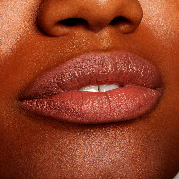 Full lips wearing All My BFFs, a warm rosy-brown nude ColourPop Lippie Pencil, lining and filling the mouth with a creamy satin finish on deep skin in a tight close-up, highlighting precise definition and smooth texture.