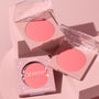 ColourPop Pressed Powder Blush Big Reveal compact displays a warm coral‑pink pan as two clear‑lid cases sit open and one boxed unit rests on a blush‑toned podium, star accents on the lids catching light for a soft, glam display.
