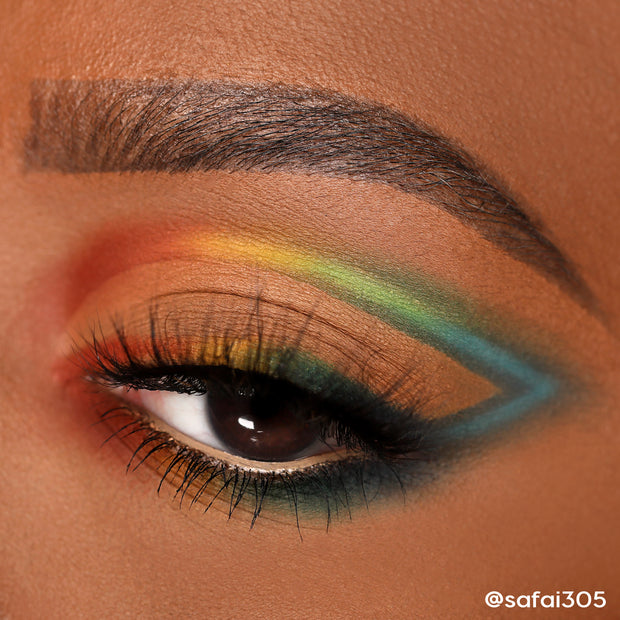 Bold matte rainbow eye makeup sweeps across a closed eyelid in a precise cut-crease and wing, blending red, orange, yellow, green, and teal to navy; lashes defined - look created with ColourPop Shadow Palette Matte About Hue.