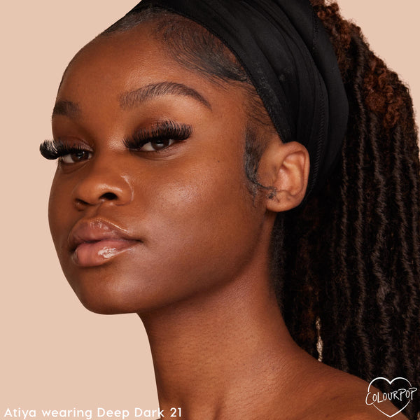 ColourPop Pretty Fresh Face Powder in Deep Dark 21 shown on a model, delivering a smooth, natural matte finish on deep skin; close-up portrait with black headband, long lashes, and glossed lips against a peach background.