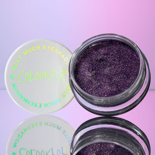 ColourPop Jelly Much Shadow Emo Inside, an open pot of deep violet, sparkle-heavy jelly eyeshadow, glistening with multicolor shimmer as the white branded lid sits beside it on a mirrored surface against a pink‑purple gradient background.