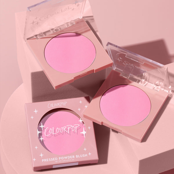 Flamingo ColourPop Pressed Powder Blush showing a vibrant bubblegum pink pan in two open square compacts with clear lids, plus one boxed unit, styled on a soft pink pedestal under studio lighting.