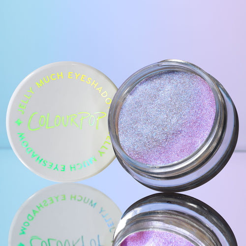ColourPop Jelly Much Shadow Hallucinogenius opens to reveal an iridescent lavender-blue jelly eyeshadow with metallic shimmer, its white lid with COLOURPOP logo beside it, mirrored on a glossy surface against a pastel blue-purple backdrop.