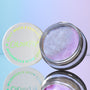 ColourPop Jelly Much Shadow Hallucinogenius opens to reveal an iridescent lavender-blue jelly eyeshadow with metallic shimmer, its white lid with COLOURPOP logo beside it, mirrored on a glossy surface against a pastel blue-purple backdrop.