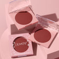 ColourPop Pressed Powder Blush Icing on Top compact opening to reveal a deep rose pan, with a second open compact and a branded box arranged on soft pink blocks under studio lighting, showcasing the warm cheek color.