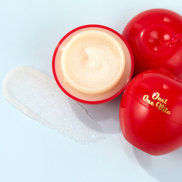 Just One Bite ColourPop Lip Scrub opens to show a creamy, shimmery sugar scrub in a red, apple-shaped jar, gold “Just One Bite” lettering on the lid, with a translucent swatch smeared on a light blue surface.