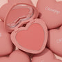 Heart-shaped Let’s Dance ColourPop Pressed Powder Blush compact opens to reveal a coral pink powder pan and built-in mirror, resting among matte pink ColourPop heart cases on a soft blush backdrop.