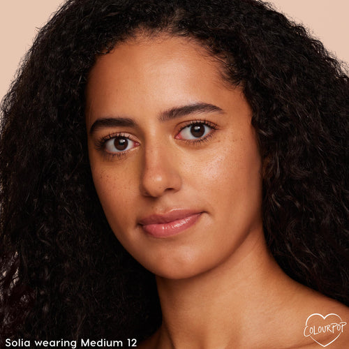 Model wearing ColourPop Pretty Fresh Face Powder in Medium 12, showcasing smooth, even coverage and a natural skin finish; close-up portrait against a neutral peach background highlighting shade match and soft-focus look for everyday wear.