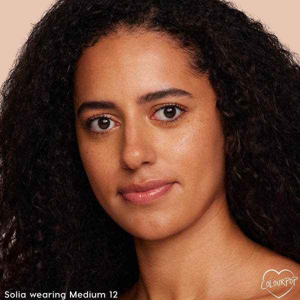 Model wearing ColourPop Pretty Fresh Face Powder in Medium 12, showcasing smooth, even coverage and a natural skin finish; close-up portrait against a neutral peach background highlighting shade match and soft-focus look for everyday wear.