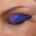 Doe-foot applicator sweeps Morpho, a ColourPop Chrome Liquid Shadow, across a closed eyelid, showing a high-shine metallic blue-to-violet duochrome finish from inner corner to outer lid with smooth, opaque coverage.