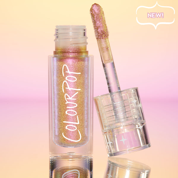 Bliss ColourPop Chrome Liquid Shadow opened, the shimmery multichrome wand resting on a clear cap with star accents, showing pink‑to‑gold‑lilac shift in a clear tube labeled ColourPop, set on a reflective peach‑to‑pink gradient backdrop with a NEW badge.