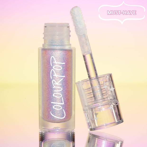 ColourPop Chrome Liquid Shadow in Glaze stands open, doe-foot applicator leaning on the iridescent tube, multichrome shimmer shifting pink, lilac, and blue, set on a pastel pink-to-yellow gradient with a “Must-Have” badge and mirrored surface.