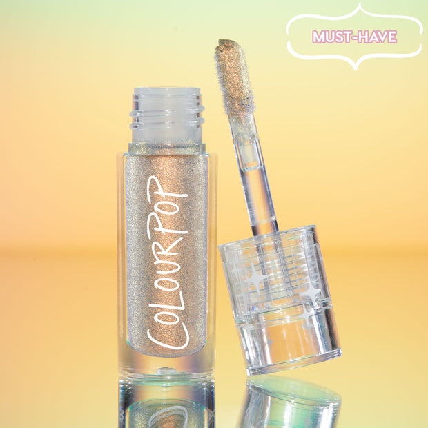 ColourPop Chrome Liquid Shadow in Sweetzer Ave stands open as the doe-foot applicator reveals a multi-chrome gold-peach sheen, the clear tube with white ColourPop logo reflecting against a mint-to-peach gradient background with a “MUST-HAVE” badge.