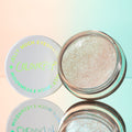 Open pot of ColourPop Jelly Much Shadow in Sage Bundle, a sparkling icy-champagne gel eyeshadow, sits beside its white lid with iridescent logo on a mirrored surface against a pastel peach-to-mint gradient.