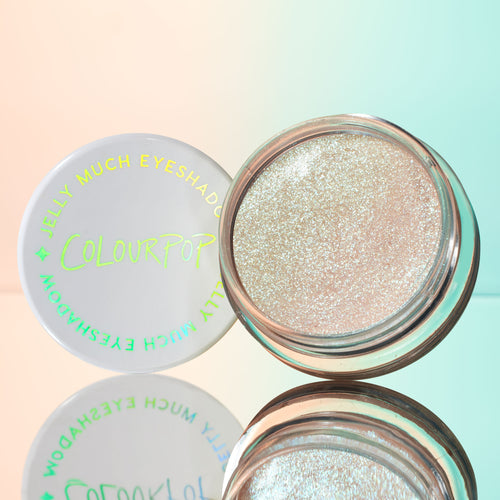 Open pot of ColourPop Jelly Much Shadow in Sage Bundle, a sparkling icy-champagne gel eyeshadow, sits beside its white lid with iridescent logo on a mirrored surface against a pastel peach-to-mint gradient.