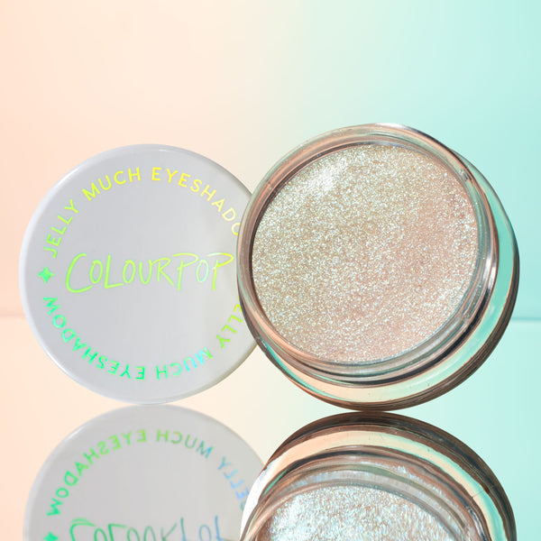 Open pot of ColourPop Jelly Much Shadow in Sage Bundle, a sparkling icy-champagne gel eyeshadow, sits beside its white lid with iridescent logo on a mirrored surface against a pastel peach-to-mint gradient.