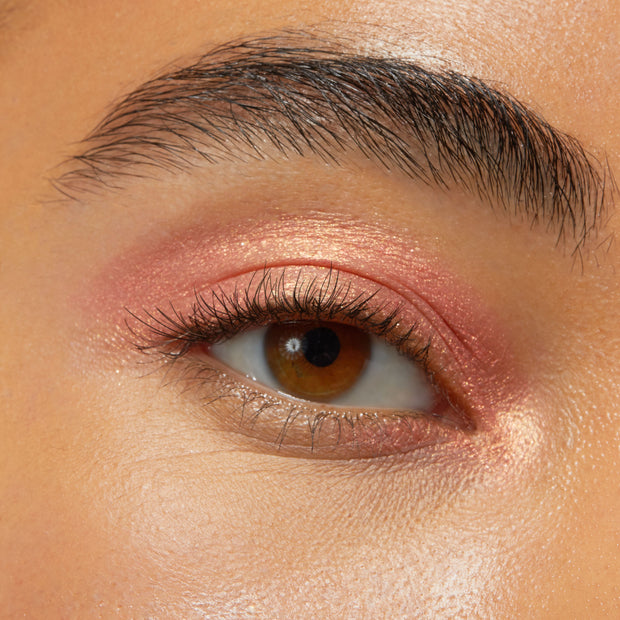 Brown eye wearing Friday Feels Shadow Stix, a shimmering rose-gold pink from the ColourPop Shadow Stix line, swept across the lid and inner corner with a soft metallic sheen in a close-up beauty swatch.